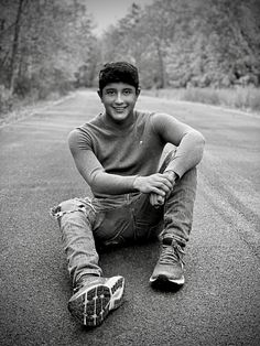 a young man sitting on the side of a road with his feet propped up in front of him