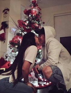 a man and woman kissing in front of a christmas tree with lights on the bottom