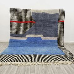 a blue and black area rug with red lines on the edges, in front of a white wall