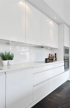 a kitchen with white cupboards and counters in the center, along with potted plants on the counter