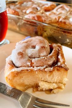 a cinnamon roll on a plate next to a fork and glass of tea with a spoon in it