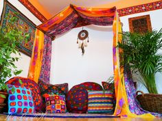 a bed covered in colorful pillows next to a potted plant and hanging dream catcher