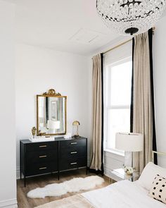 a bedroom with white walls, black dressers and a chandelier hanging from the ceiling