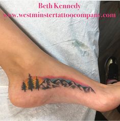 a person with a tattoo on their foot that has mountains and trees in the background