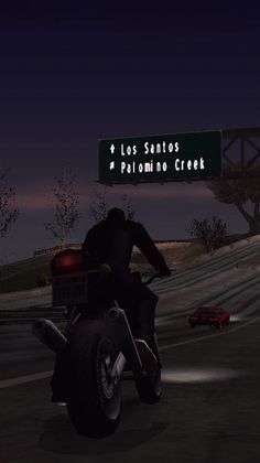 a man riding on the back of a motorcycle next to a street sign at night