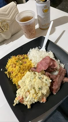 a black plate topped with meat and rice next to a cup of tea on a table