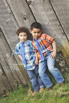 two young boys standing next to each other in front of a wooden fence with grass