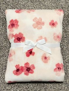 a pink and white flowered blanket with a bow on it's end laying on the floor