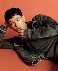 a young man sitting on the floor with his hand under his chin