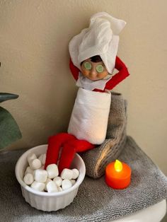 an elf is sitting on a stool with marshmallows in front of him