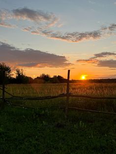 the sun is setting over a field with a fence and trees in the foreground