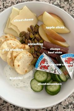 a white bowl filled with crackers, apples, cucumbers and other foods