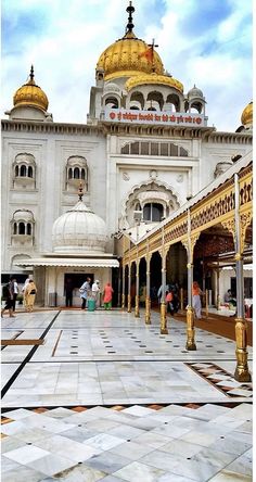 an ornate white building with gold domes on it's sides and people walking around