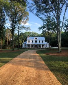 a large white house sitting on top of a lush green field next to tall trees