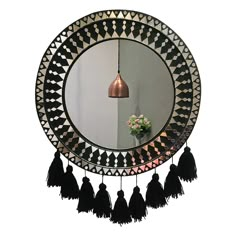 a round mirror with tassels hanging from it's sides and a vase on the other side