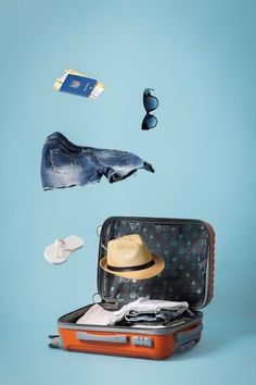 an open suitcase with clothing and hat flying out of it on a blue background,