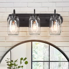 three mason jar lights are hanging from the ceiling above a mirror in a room with brick walls