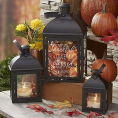 three black lanterns sitting on top of a wooden table next to flowers and pumpkins