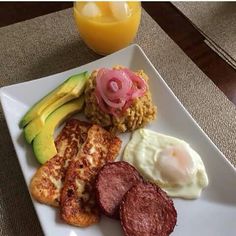 a white plate topped with meat, eggs and other foods next to a glass of orange juice