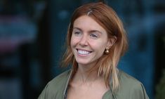 a woman with red hair is smiling at the camera while wearing an army green shirt