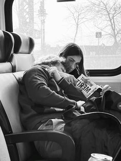 a woman sitting on a bus reading a book while holding a baby in her lap