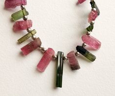 a necklace with pink, green and silver beads on a white background is shown in the foreground