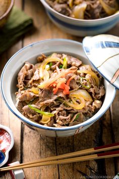 a bowl filled with meat and vegetables next to chopsticks on a wooden table