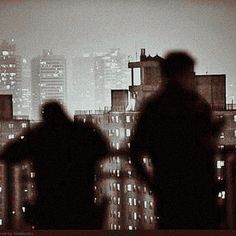 two people standing on top of a building at night with city lights in the background