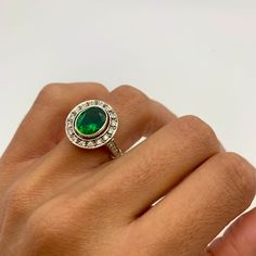 a woman's hand holding a ring with a green stone and diamond accents on it