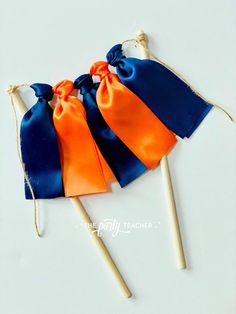 three orange and blue candy bags on top of toothpicks with ribbons tied around them