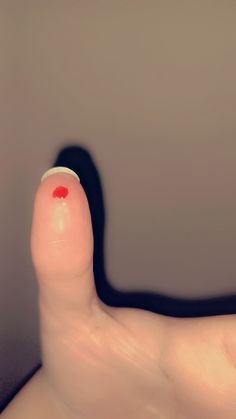 a person's finger with a red spot on the tip of their thumb in front of a gray wall