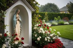 a statue of the virgin mary in a garden with flowers around it and a dog house