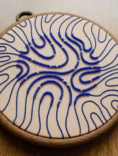 a blue beaded design is on a white piece of wood with a black thread