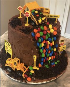 a large chocolate cake with construction trucks and candy on the top is sitting on a table