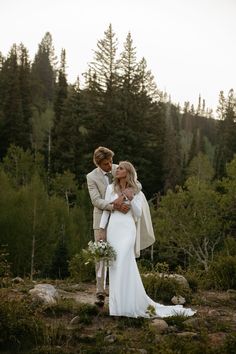 a bride and groom standing in the woods