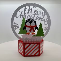 a penguin is sitting on top of a box with christmas decorations around it and the words merry christmas