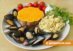 a white plate topped with mussels, tomatoes and other foods on top of a wooden table