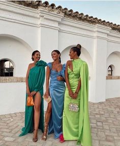 three women in dresses standing next to each other near a white building with arches on it