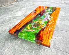 a colorful glass table sitting on top of a cement floor next to a tree trunk