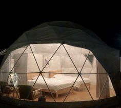 the inside of a dome tent with a bed and chairs in it at night time