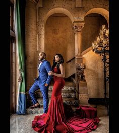 a man and woman standing next to each other in front of a staircase with chandeliers