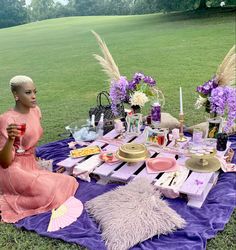 a woman sitting at a picnic table with food and drinks in front of her on the grass