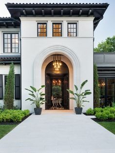 a large white house with an arched doorway and green trim on the front door is surrounded by greenery