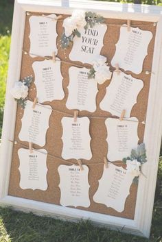 a cork board with seating cards attached to it and flowers on the top, sitting in grass