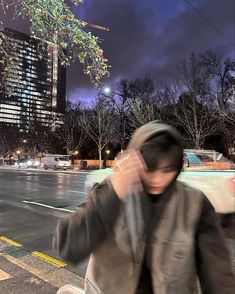 a man is sitting on the curb talking on his cell phone while wearing a hoodie