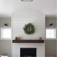 a fireplace with a wreath on the mantle and two lights above it in a living room