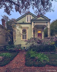 a green house with pink flowers in the front yard and brick walkway leading up to it