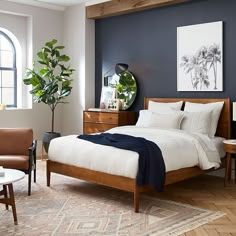 a bed room with a neatly made bed next to a chair and a potted plant