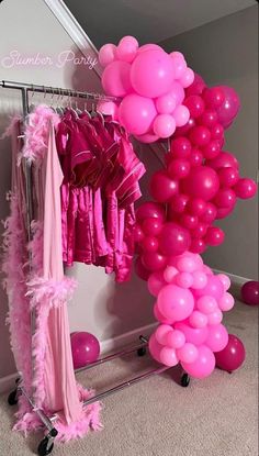 some pink balloons are hanging from a rack in front of a mirror and clothes on hangers