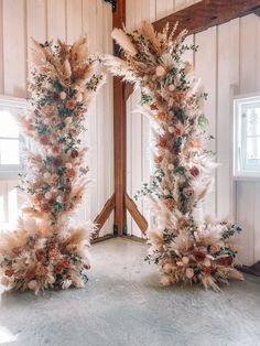 two tall floral arrangements in the middle of a room with white walls and wooden beams